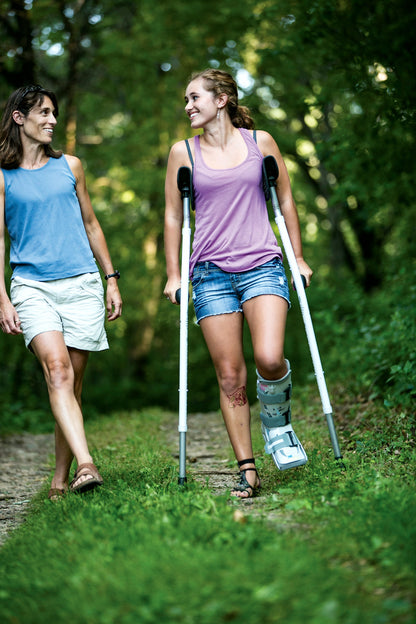 A Mobilegs Ultra user walking a wooded trail with a friend, wearing a walking boot